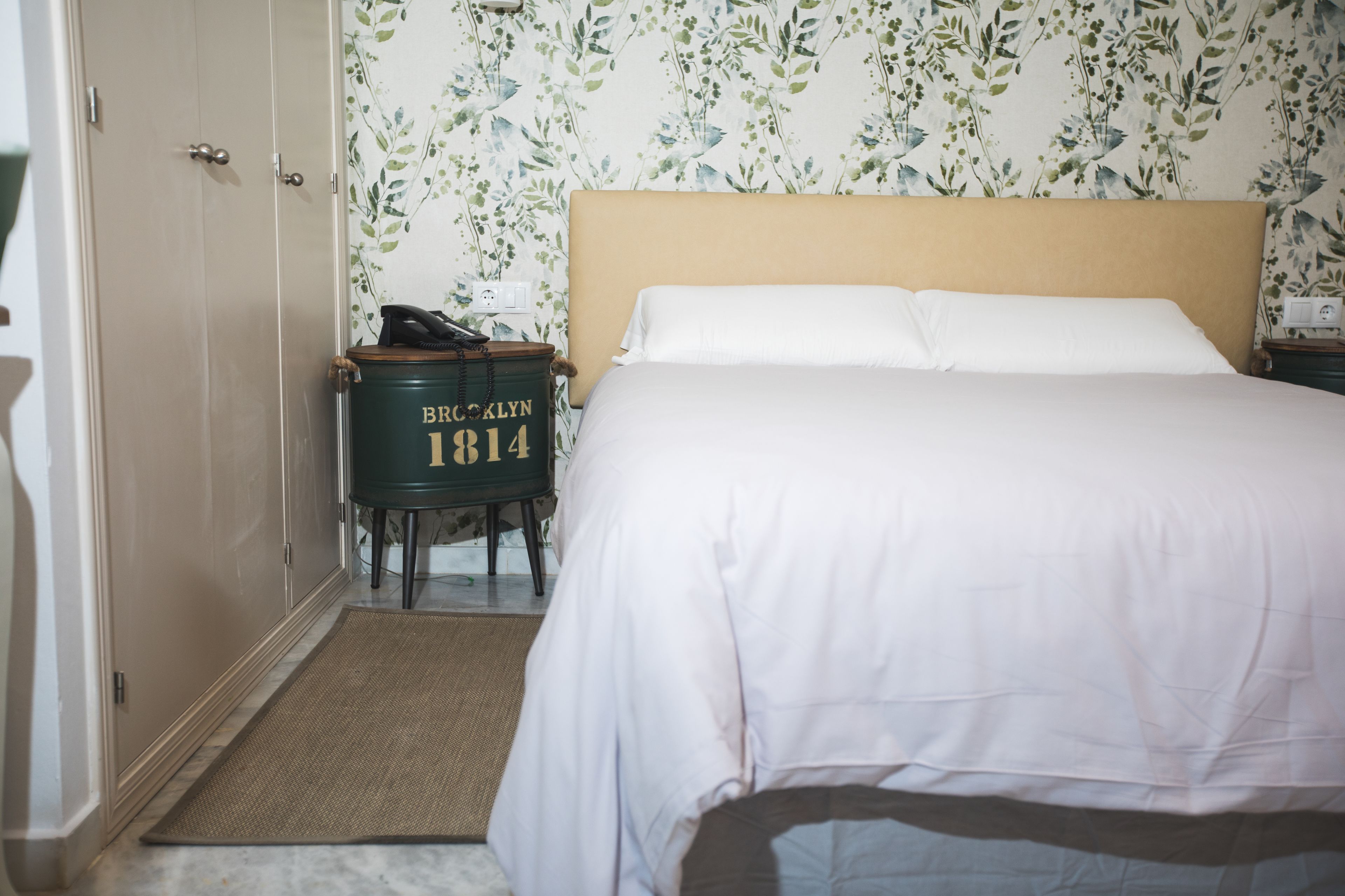 Une chambre à coucher avec un lit, une table de chevet, une commode et un papier peint à motifs floraux.
