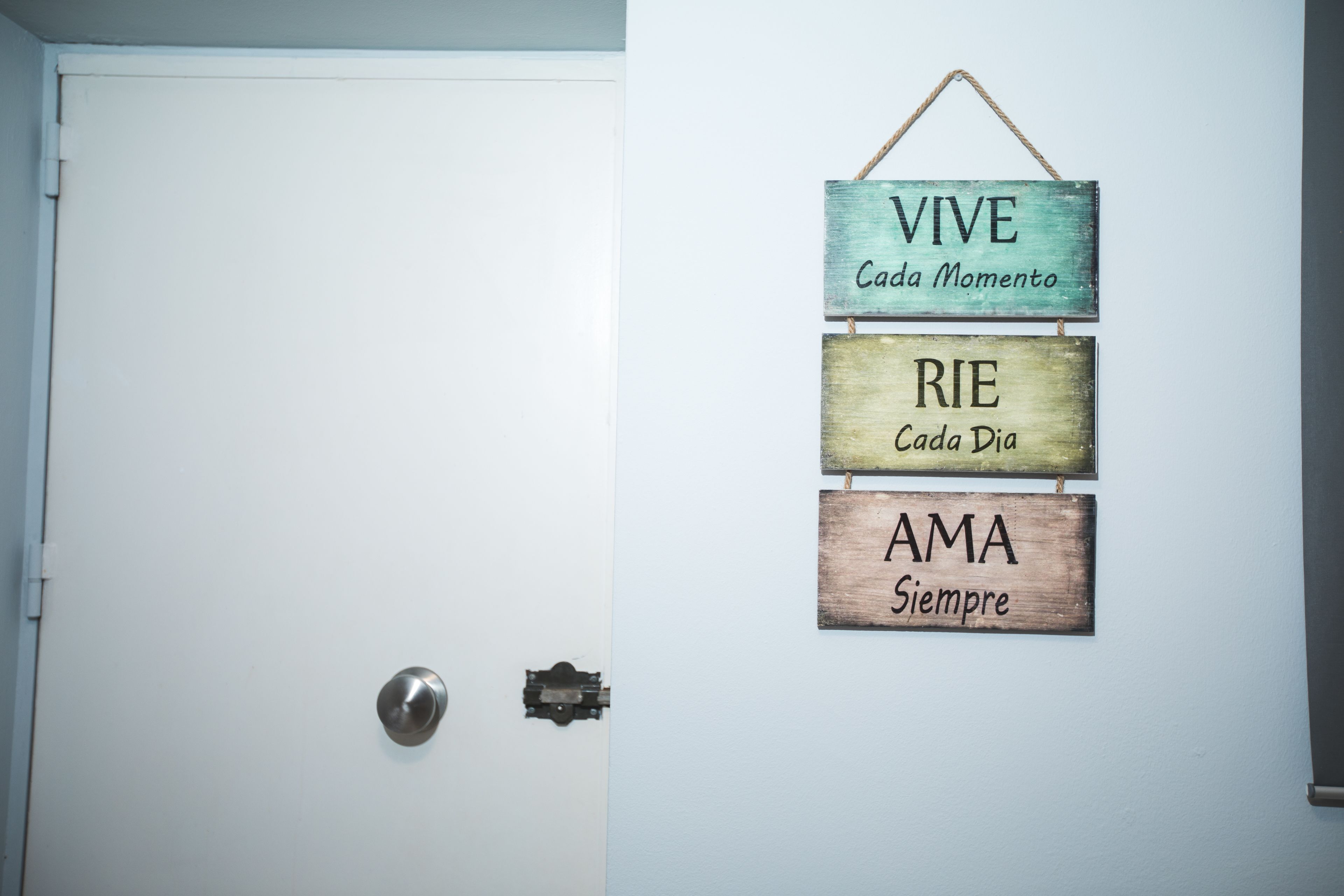 Une porte avec une pancarte sur le mur où l’on peut lire : « VIVE Cada Momento », « RIE Cada Dia » et « AMA Sempre ».