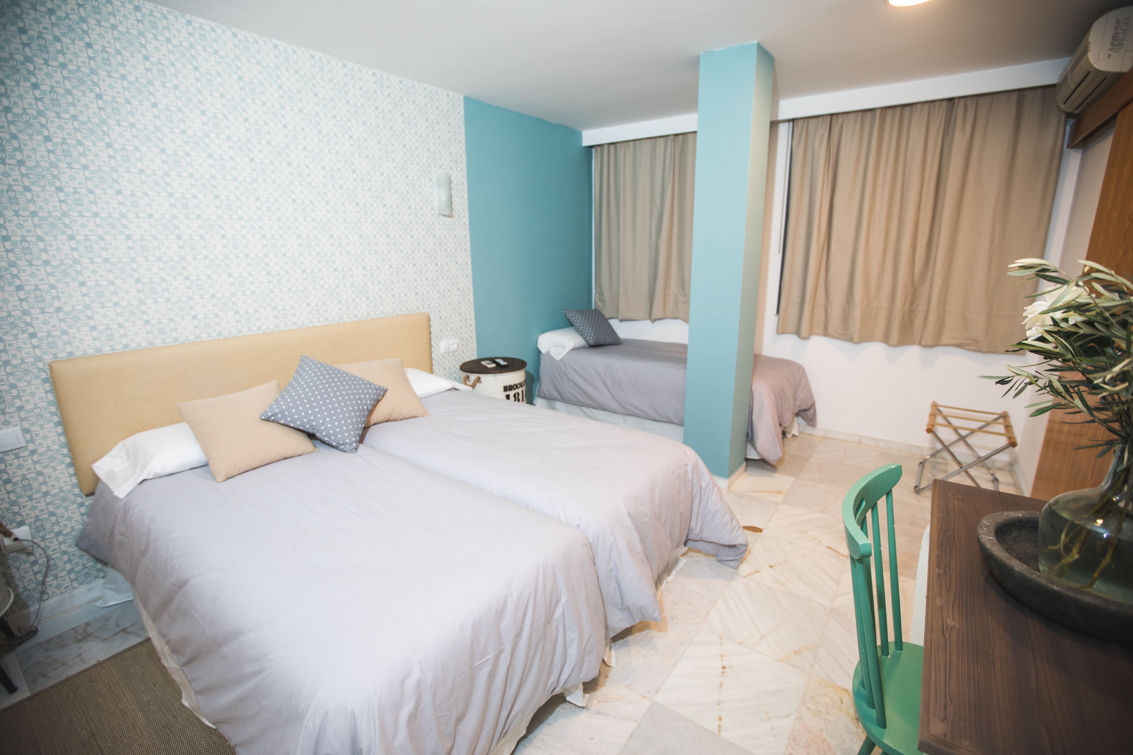 Ein Hotelzimmer mit zwei Betten, einem Schreibtisch, einem Stuhl und einer Topfpflanze.