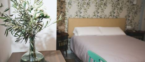 A room with a bed, a nightstand, a green chair, and a vase with flowers on a table.