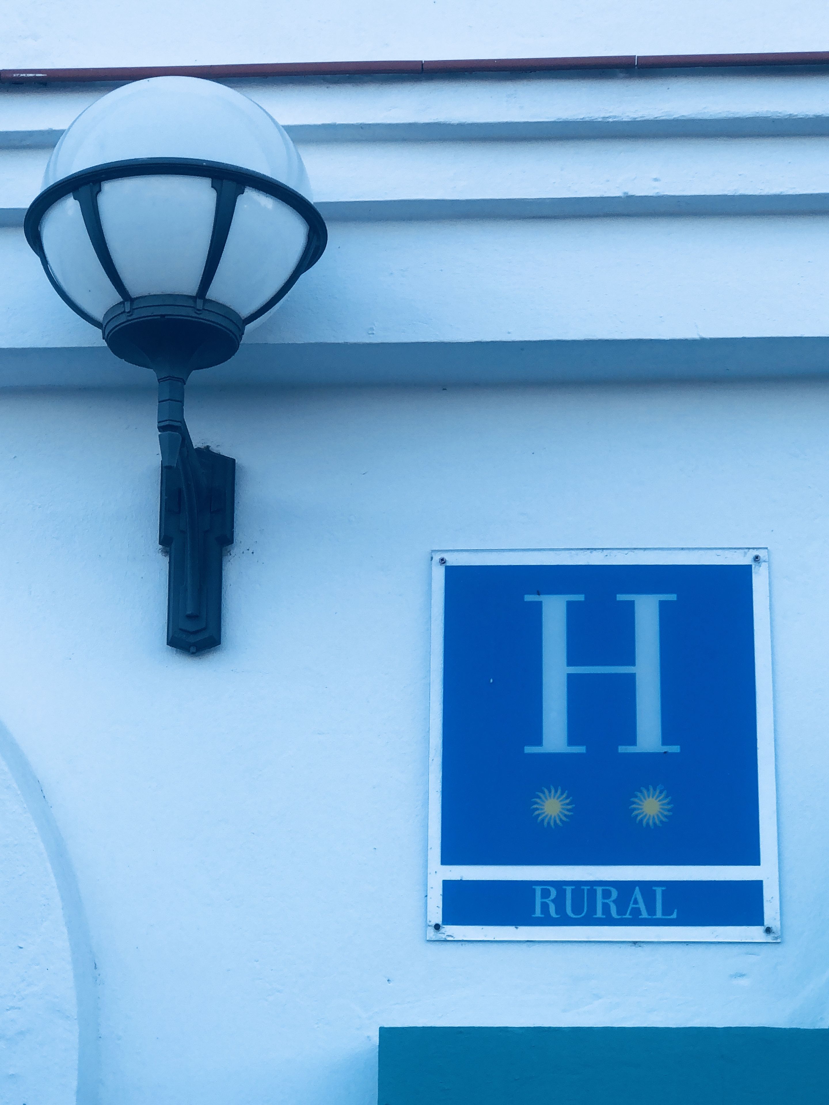 A building with a blue sign that reads "H RURAL" and a street lamp attached to the wall.