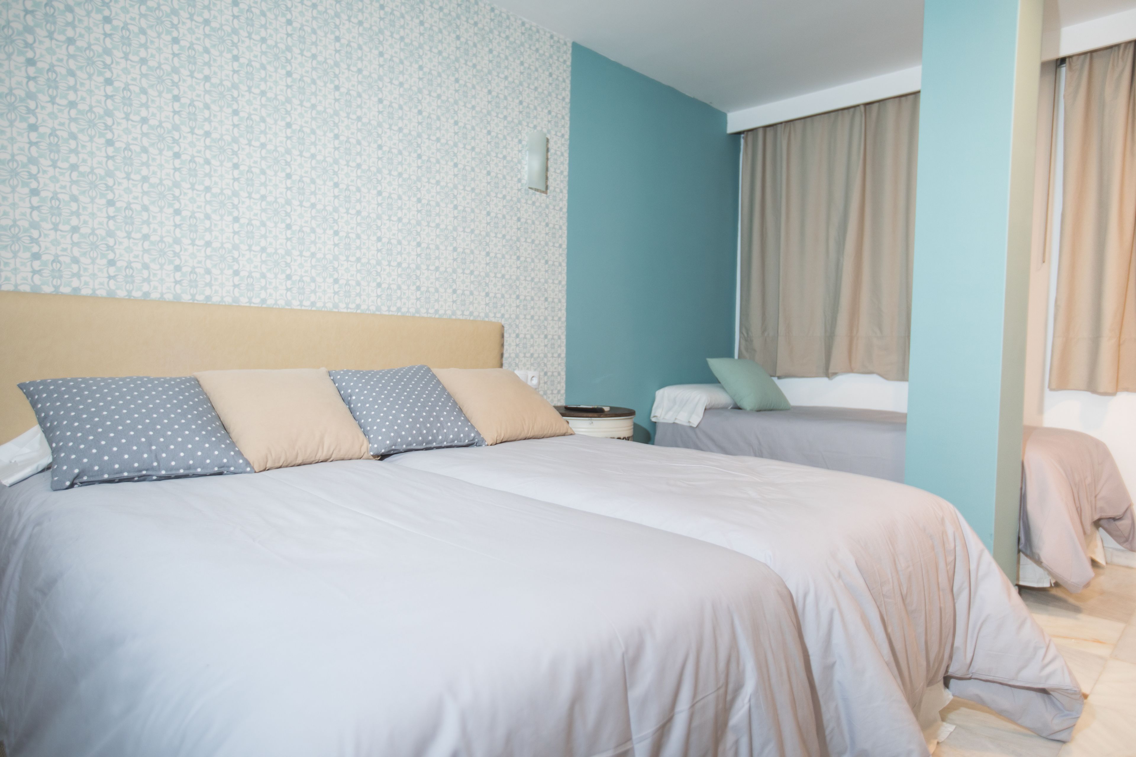 A hotel room with two beds, a patterned wallpaper, and a view of the outside.