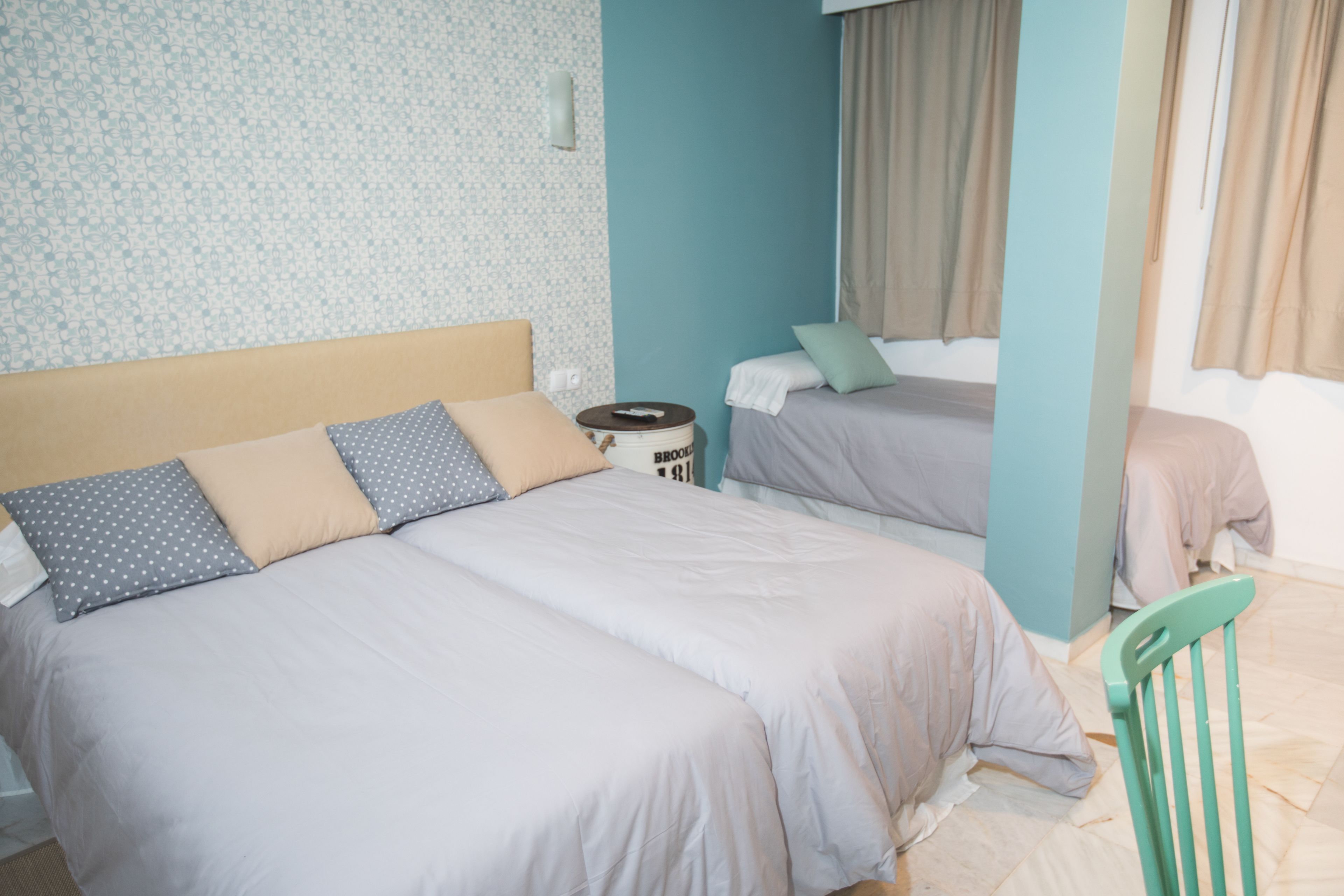 Habitación de hotel con dos camas, una silla de madera y una mesita con un control remoto.