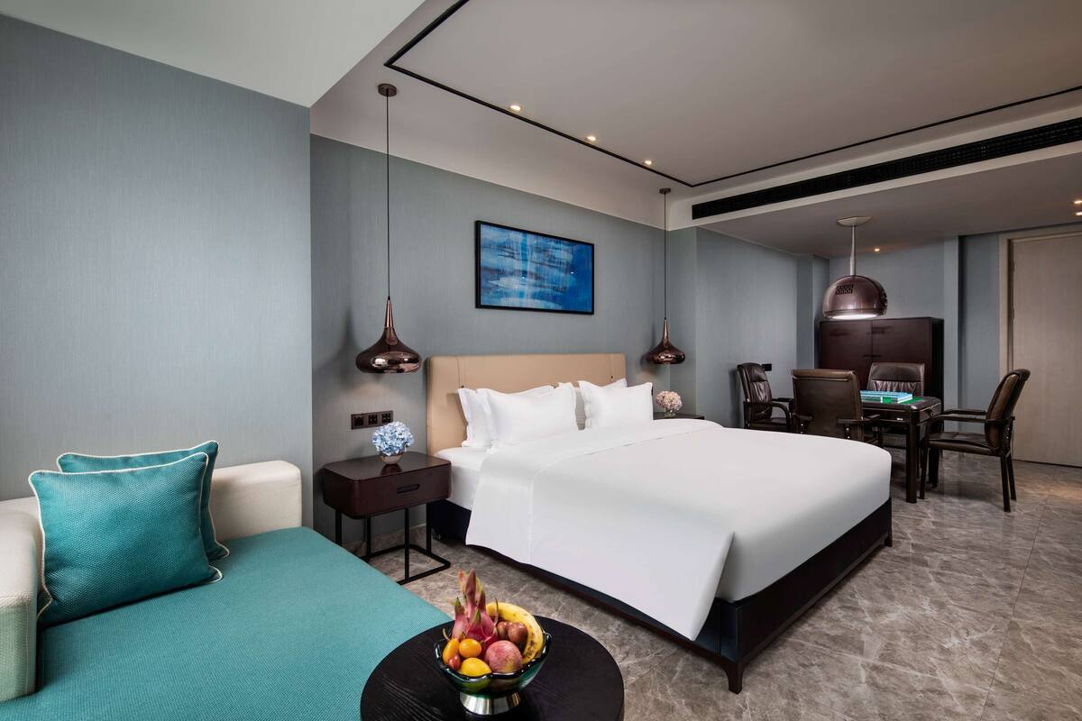 A modern hotel room with a large bed, a desk, and a seating area.
