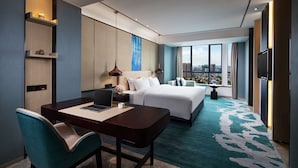 Una habitación de hotel moderna con una cama grande, un escritorio con una computadora portátil, una silla y vistas a la ciudad a través de amplios ventanales.