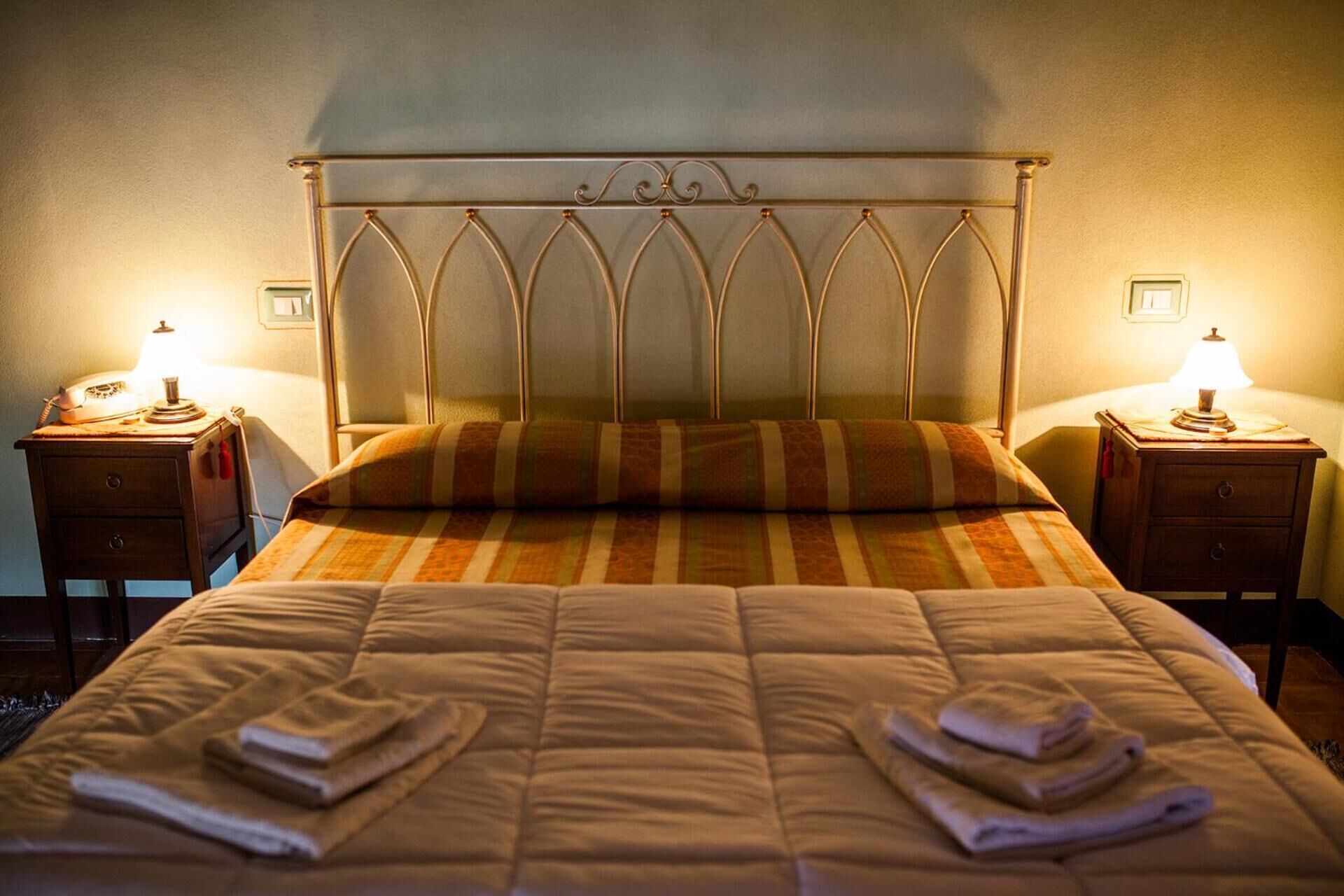 Een keurig opgemaakt bed met een gestreept kussen en twee bedlampjes op houten nachtkastjes.