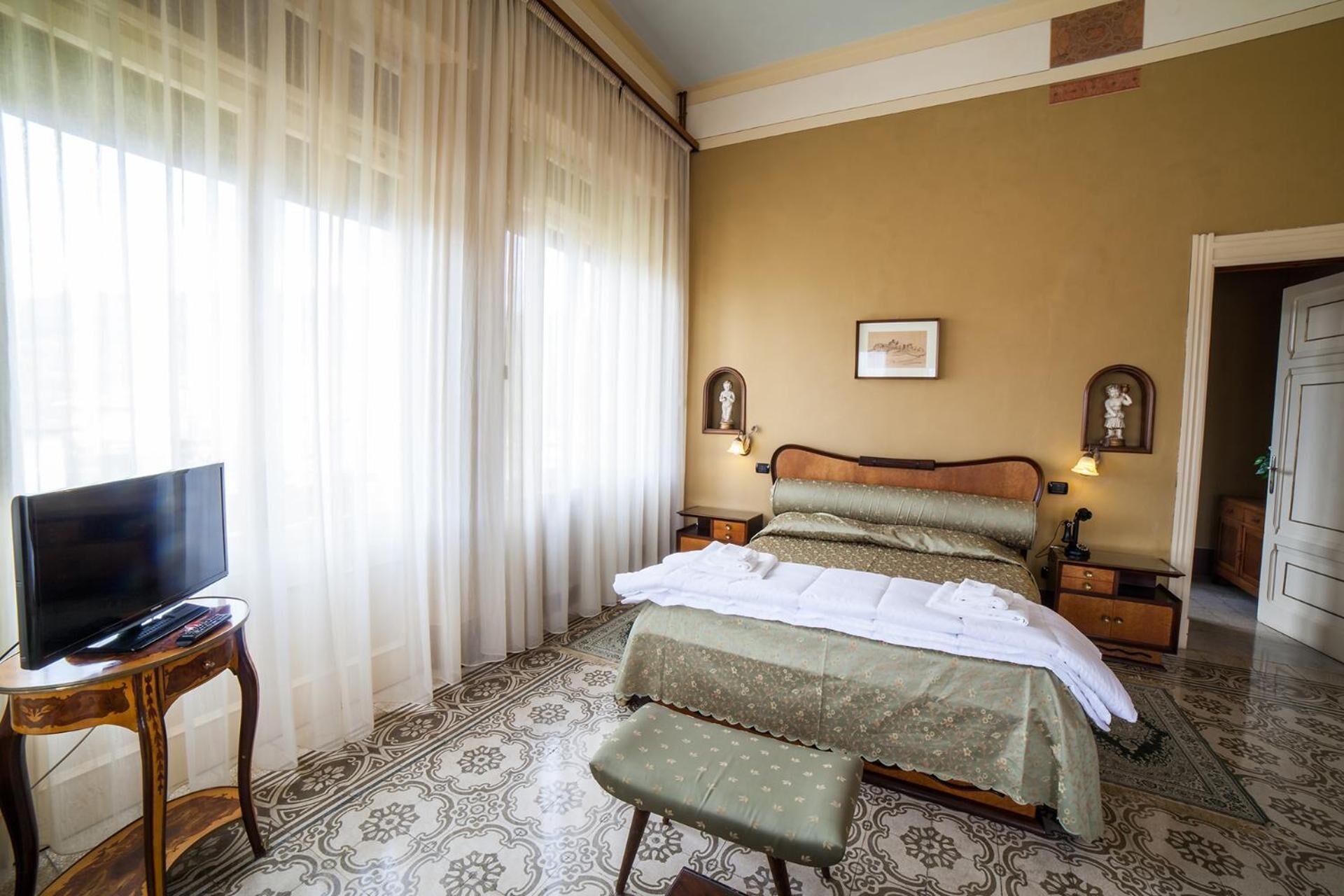 Una habitación de hotel con una cama, mesitas de noche, un televisor y un banco.