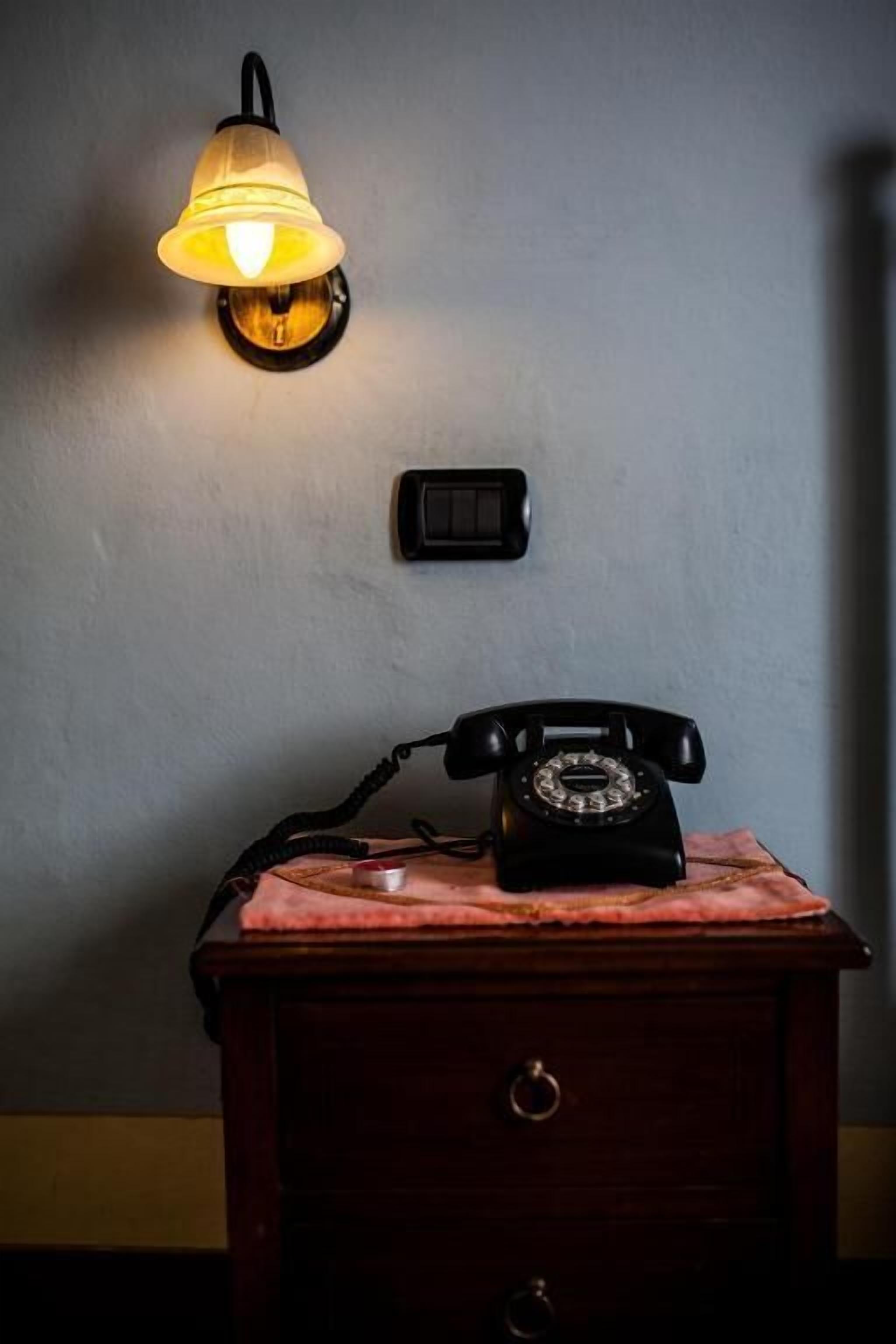 Ein altes Telefon auf einem Nachttisch aus Holz, darüber eine Lampe.