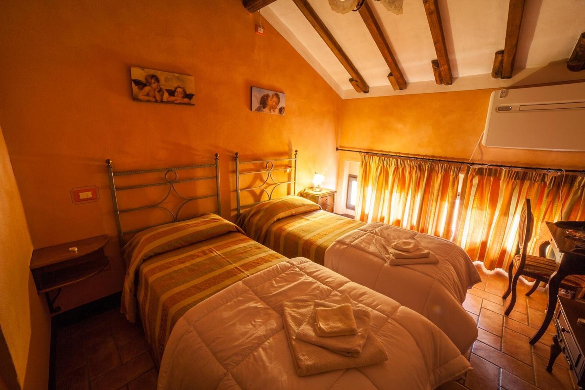 A room with two beds, a wooden ceiling, and a window with curtains.