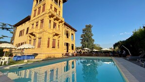 A large building with a pool in front, surrounded by outdoor seating and umbrellas. - Villa Moorings (Barga)