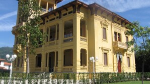 A large, yellow building with multiple balconies and columns, surrounded by a well-maintained garden. - Villa Moorings (Barga)
