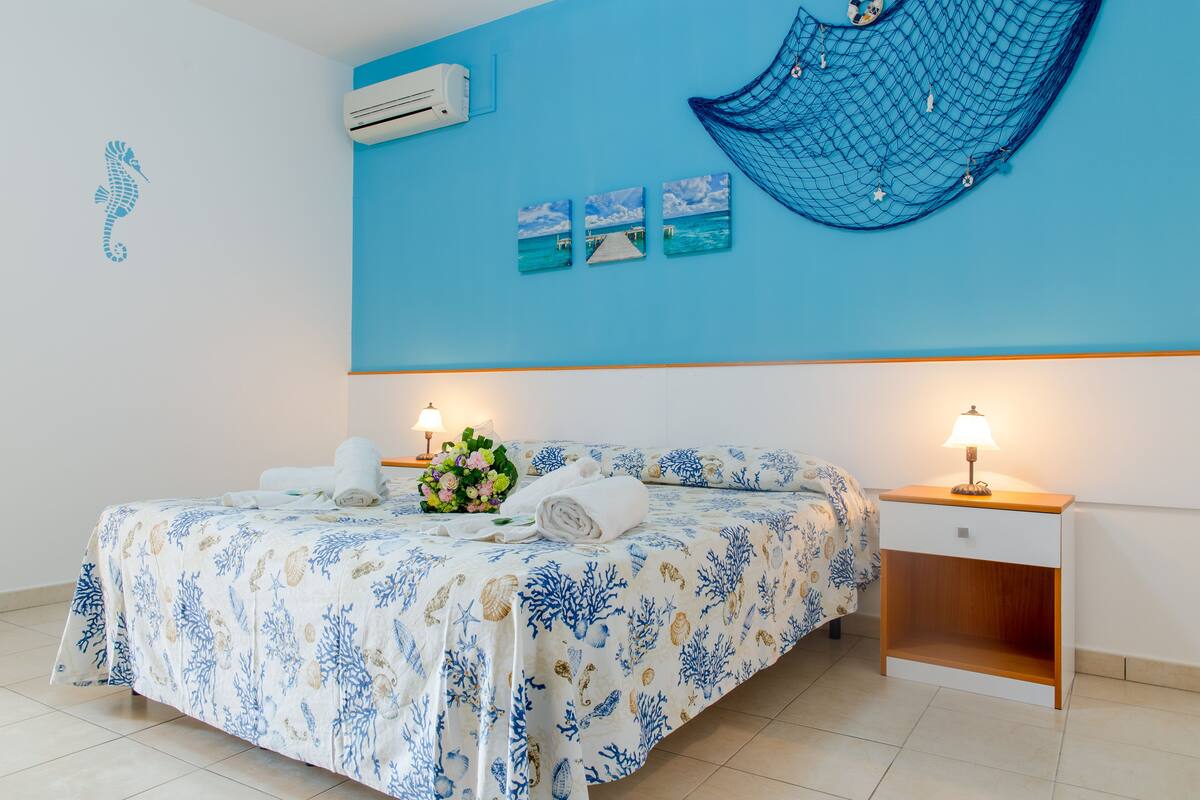 A bedroom with a bed, bedside tables, and wall decorations including a seahorse, a hammock, and three framed pictures.