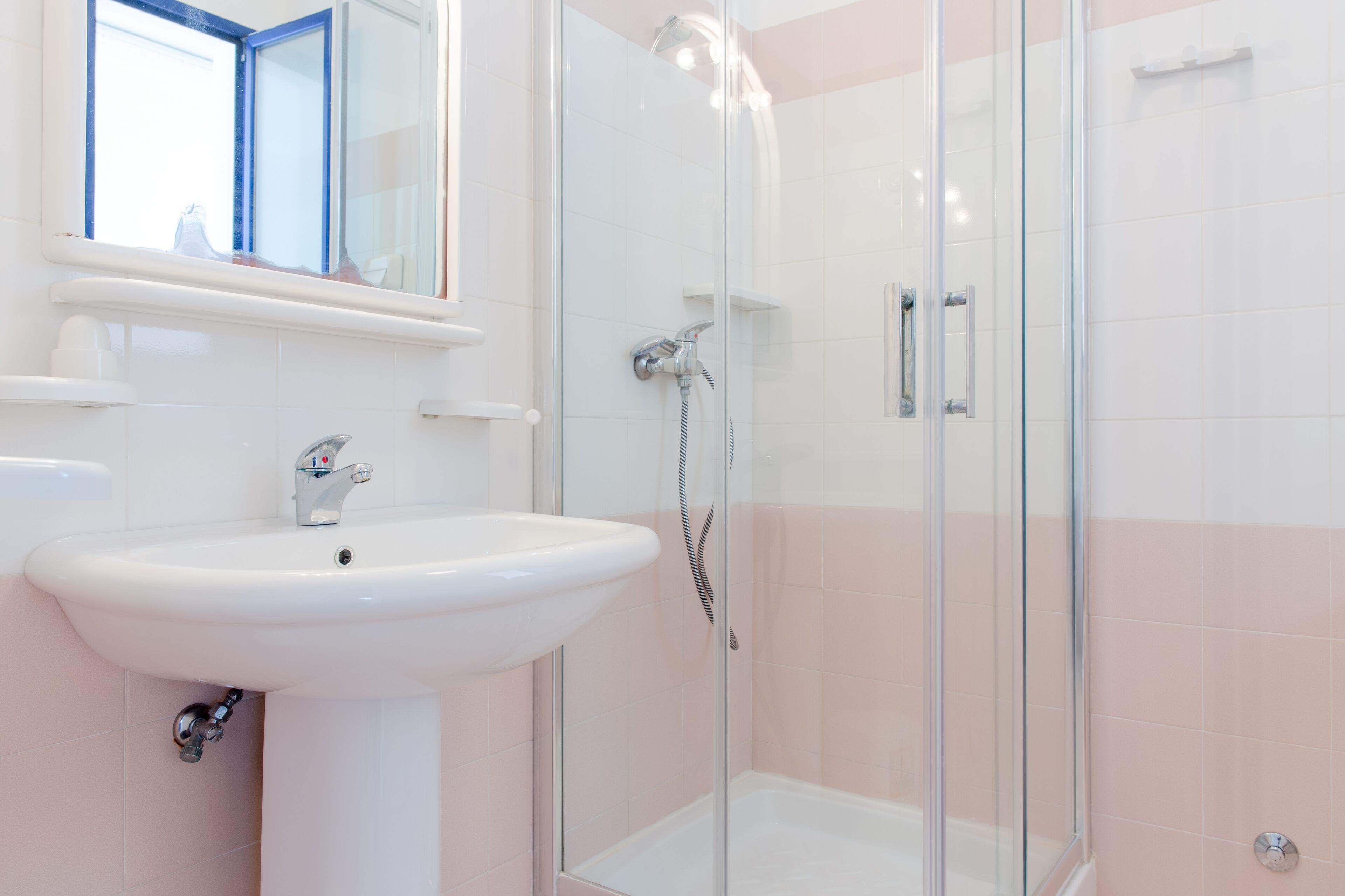 Une salle de bain avec un lavabo blanc, une cabine de douche en verre et un miroir au-dessus du lavabo.