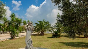 A statue in a landscaped garden with palm trees and a clear sky. - Scialabà (Salve)