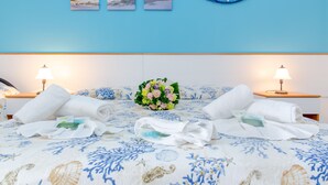 A hotel room with a bed featuring a floral bedspread, two bedside lamps, a bouquet of flowers, and a wall with three framed pictures. - Scialabà (Salve)