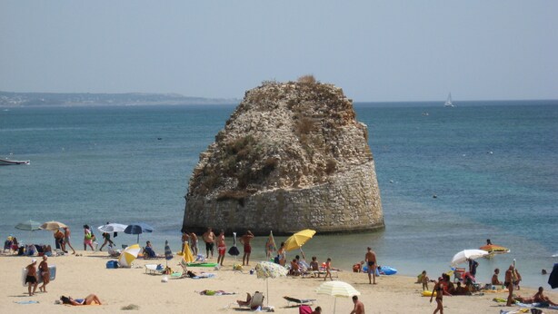 A beach with people sunbathing, umbrellas, and a large rock formation in the water. - Scialabà (Salve)