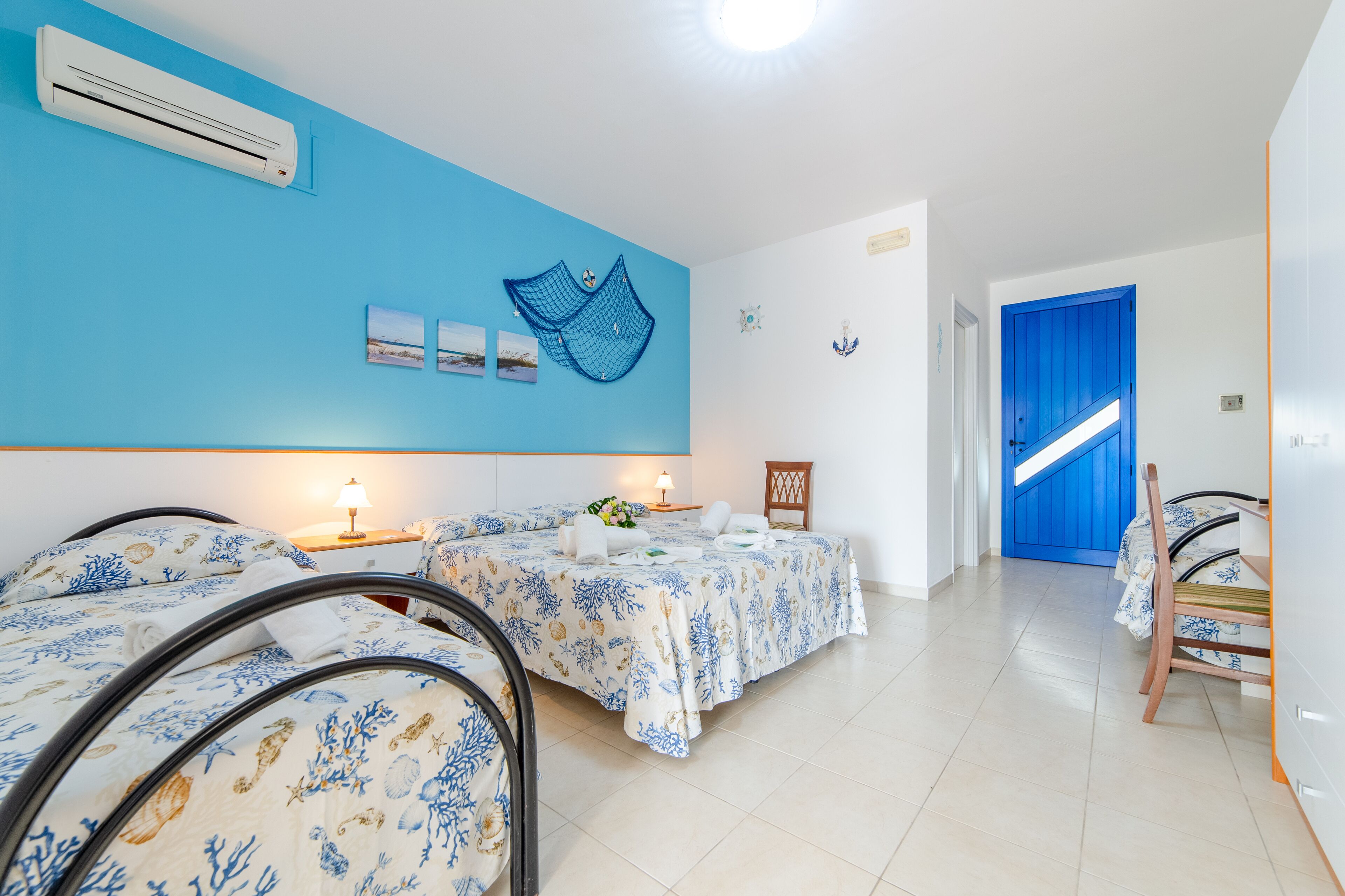 A hotel room with two beds, a blue wall, and a staircase leading to a blue door.
