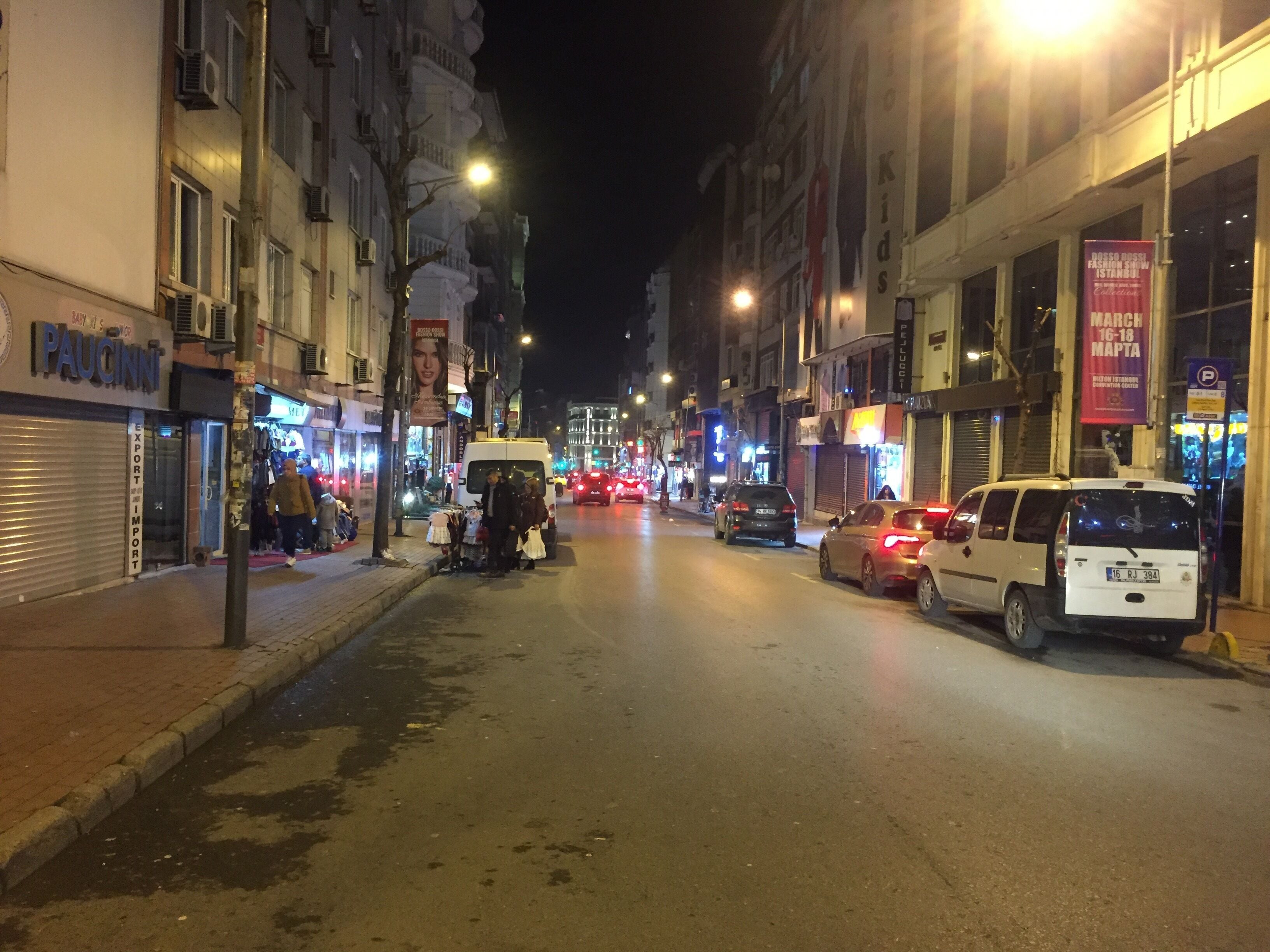 A nighttime street scene with shops and parked cars.