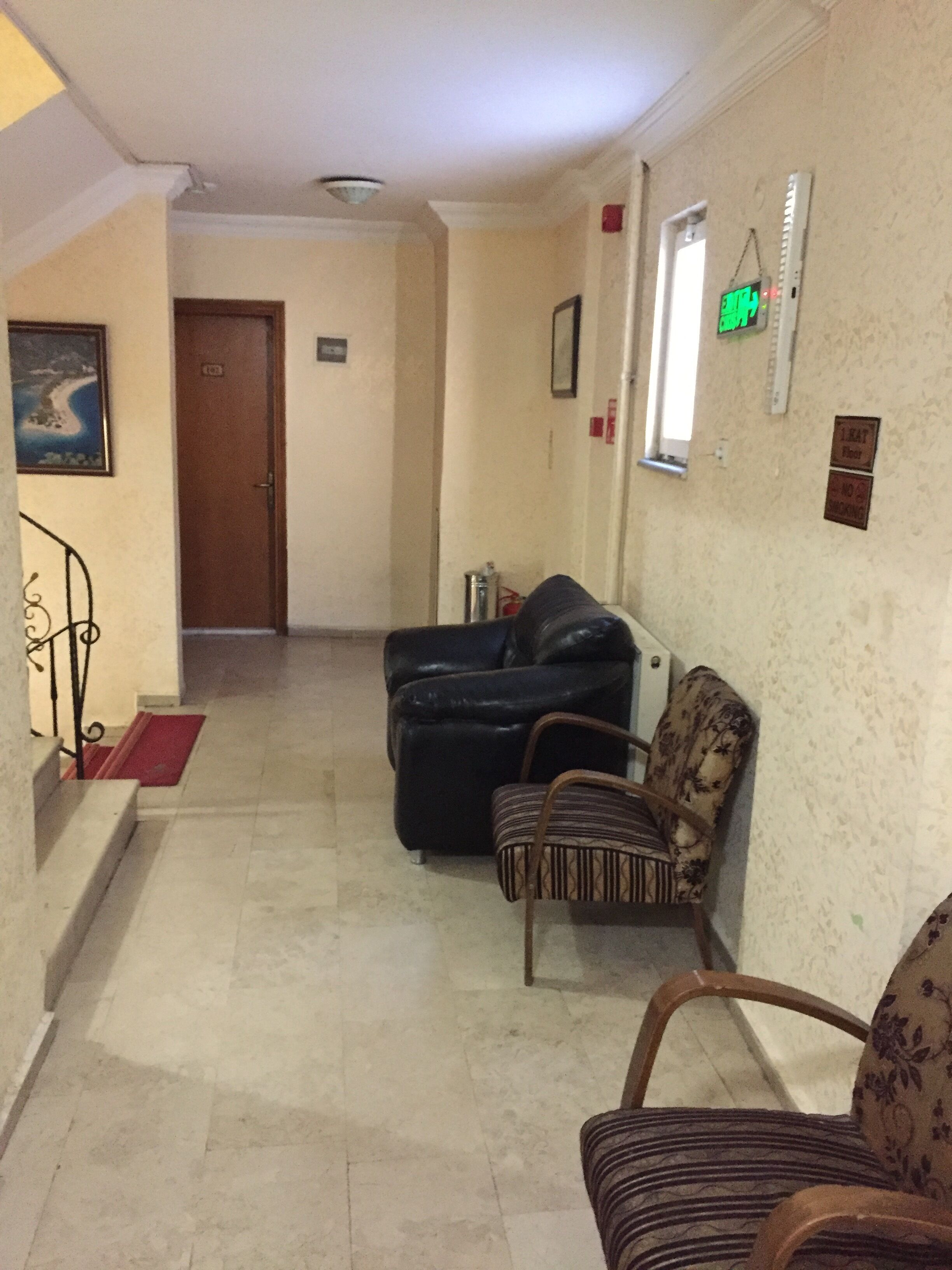 Un couloir avec un escalier menant à une porte, un canapé en cuir noir, un fauteuil à motifs et une petite table avec une chaise.