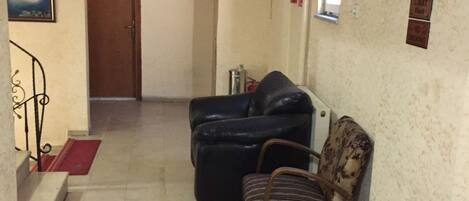 Un couloir avec un escalier menant à une porte, un canapé en cuir noir, un fauteuil à motifs et une petite table avec une chaise.
