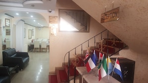 A hotel reception area with a staircase, flags, and a sign indicating room check-out time. - Florin Hotel (Istanbul)