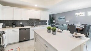 Una cocina moderna con armarios blancos, lavavajillas y un comedor con mesa y sillas.