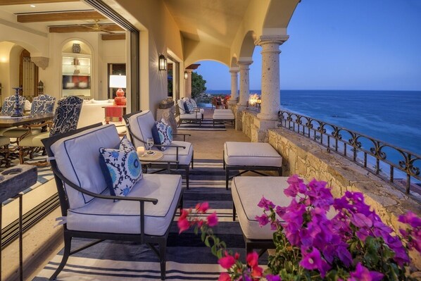 A seaside patio with outdoor seating, a view of the ocean, and a stone balustrade.