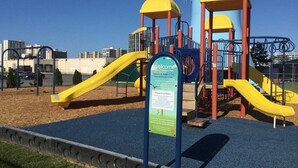 Ein Spielplatz mit gelben Rutschen und Klettergerüsten, umgeben von einem blauen Spielbereich und einem Hinweisschild.