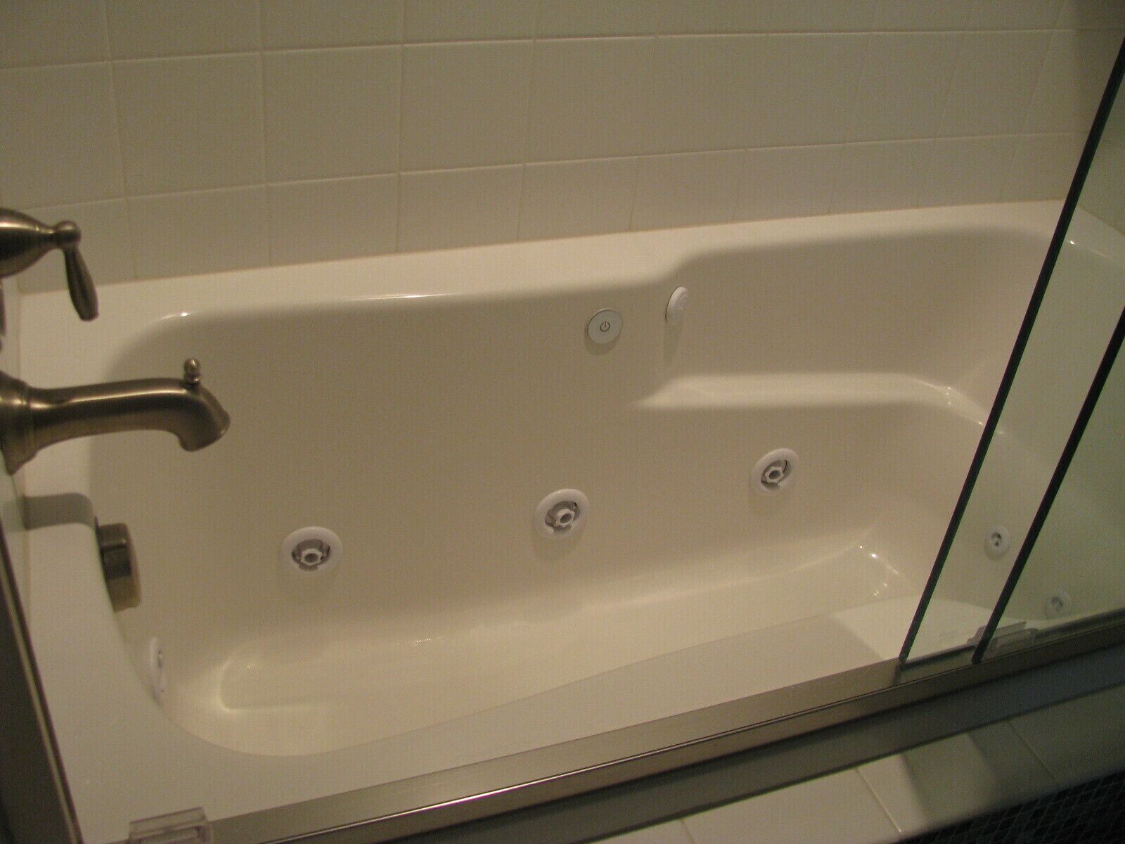 A white bathtub with a glass door, a faucet, and three drain holes.