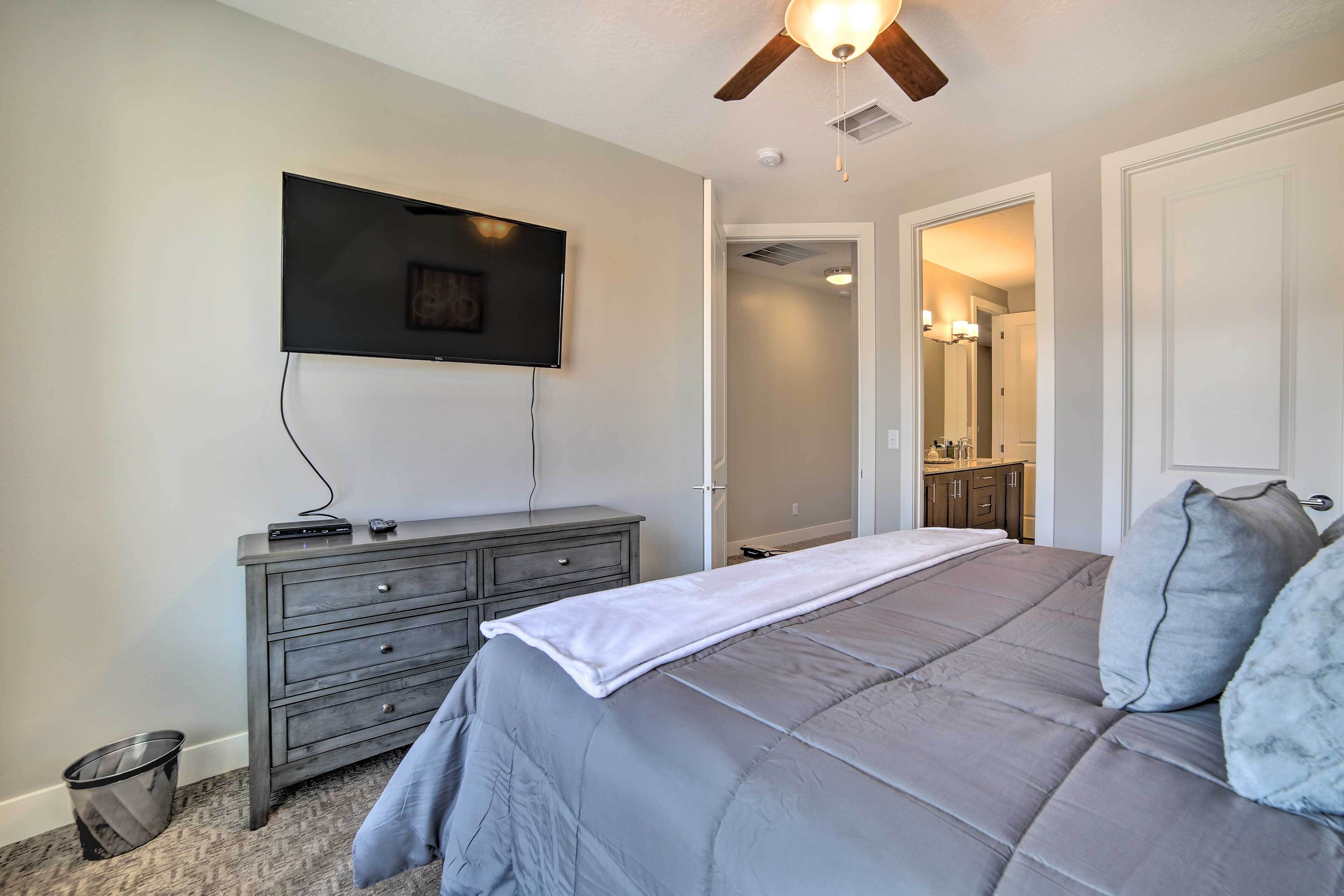 Une chambre à coucher comprenant un lit, une commode, un téléviseur fixé au mur et un ventilateur de plafond.