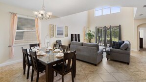 Amplia sala de estar con una mesa de comedor preparada para cuatro personas, un sofá gris y un ventanal con vistas al exterior.
