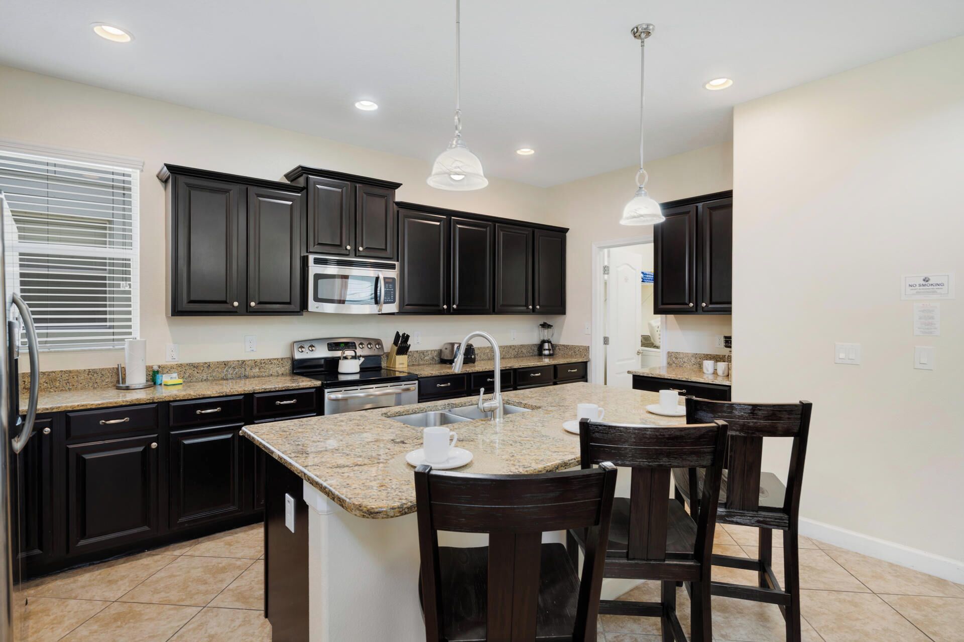 A modern kitchen with dark cabinetry, granite countertops, stainless steel appliances, and pendant lighting.