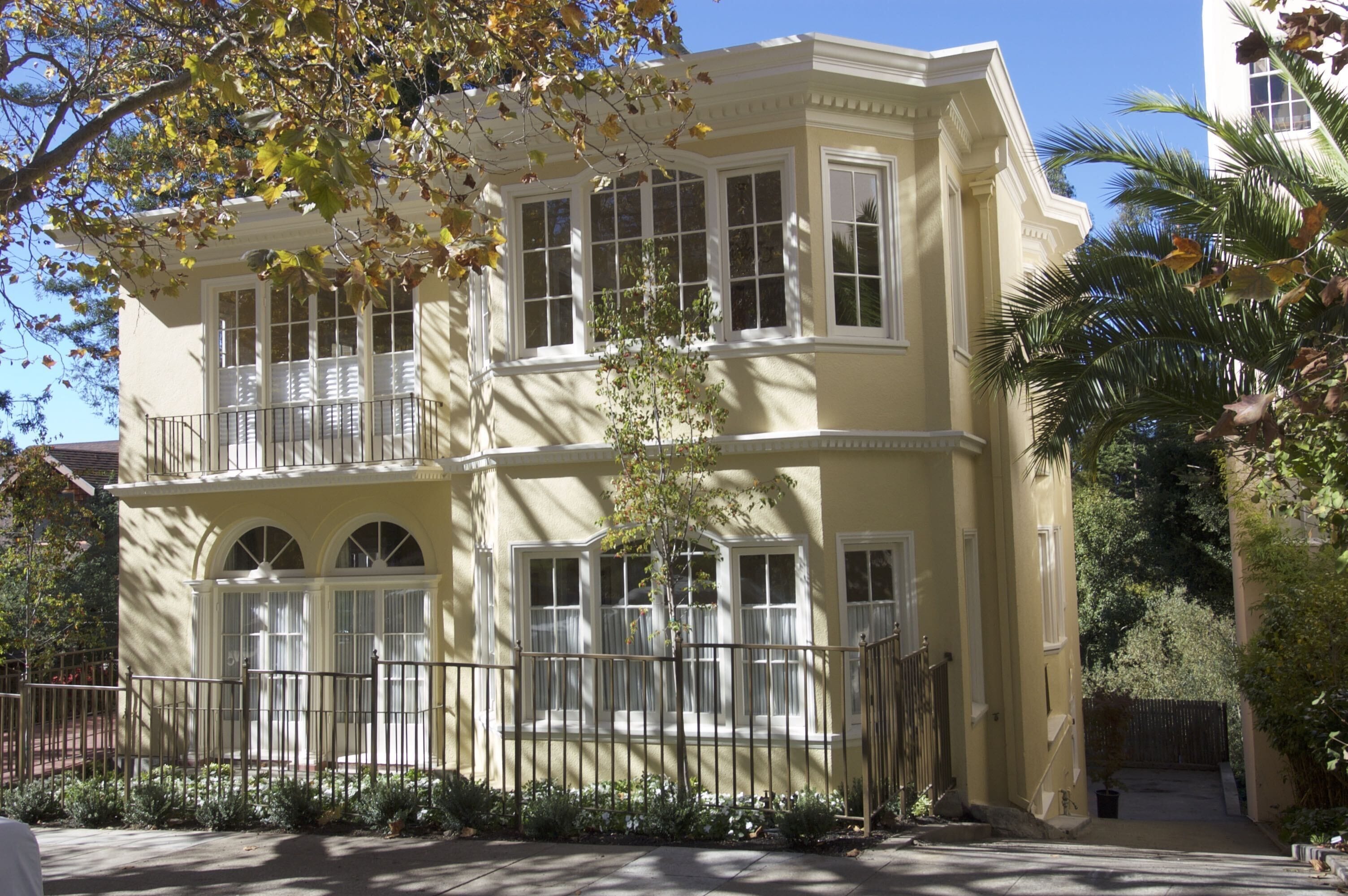 A two-story building with a balcony on the second floor, a gated entrance, and a small garden area.