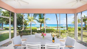 A spacious room with a large table and chairs, a ceiling fan, and large windows offering a view of the ocean and palm trees. - Northern Lights #5: 2-Story Townhome w/Backyard Snorkeling, Shared Pool + Dock (Old Man Bay)