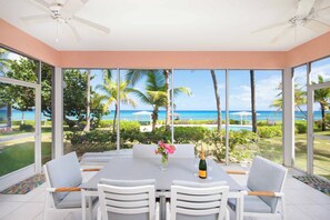 A spacious room with a large table and chairs, a ceiling fan, and large windows offering a view of the ocean and palm trees.