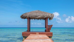 A wooden pier leading to a thatched-roof structure over clear turquoise water. - Northern Lights #5: 2-Story Townhome w/Backyard Snorkeling, Shared Pool + Dock (Old Man Bay)