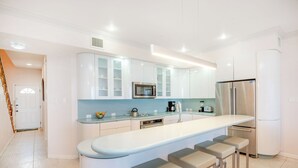 A modern kitchen with white cabinetry, a stainless steel refrigerator, a microwave, and a coffee maker. There are three bar stools at the island. - Northern Lights #5: 2-Story Townhome w/Backyard Snorkeling, Shared Pool + Dock (Old Man Bay)