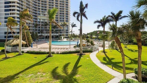 A hotel with a pool, palm trees, and a curved building facade. - Beachfront 2BR/2BA condo with pool, wifi, and Marco Island views. (Marco Island)