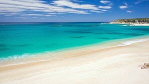 Una playa con agua turquesa cristalina, una orilla arenosa y una línea de costa distante con edificios.