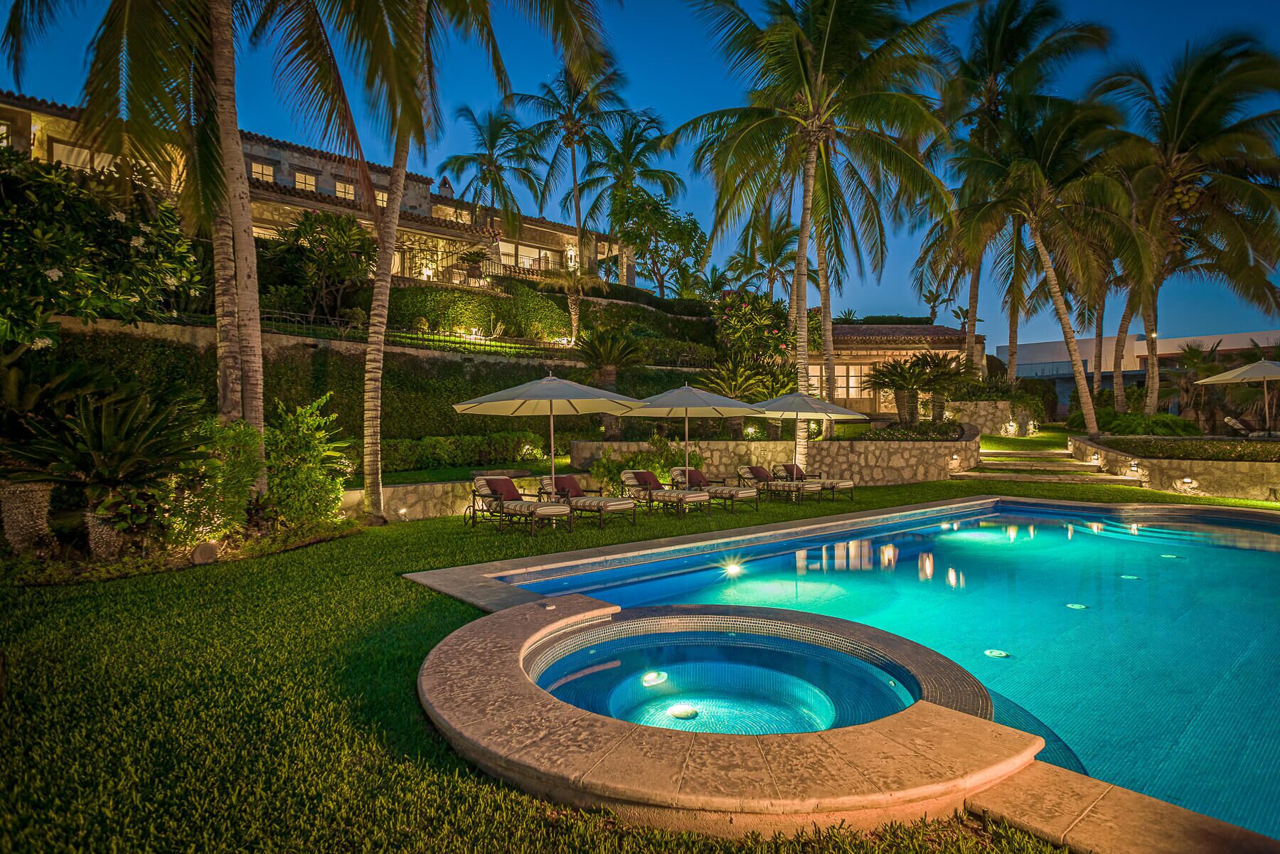 Une piscine avec un jacuzzi, entourée de palmiers et de chaises longues.