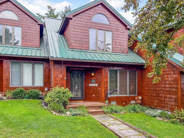 A two-story house with a green metal roof, a front porch, and a well-maintained lawn.