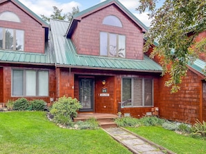 A two-story house with a green roof, a front porch, and a well-maintained lawn.