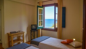Une chambre avec deux lits, une petite table avec un téléviseur et une fenêtre donnant sur la mer.