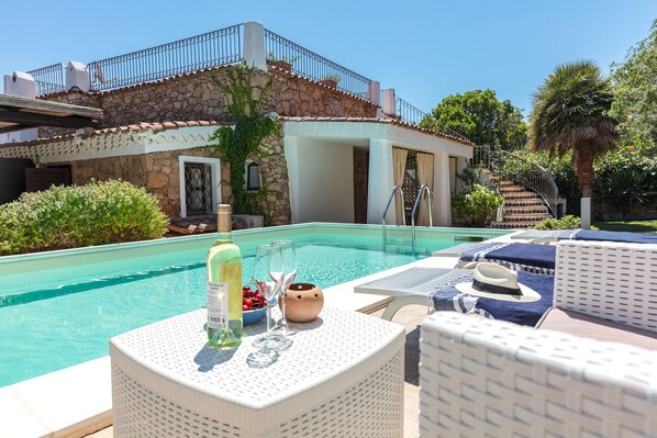 A pool area with lounge chairs, a bottle of wine, and a bowl of cherries.