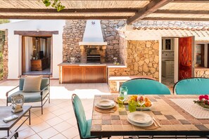 An outdoor patio with a stone wall, a built-in grill, and a dining table set with plates and glasses. - Wonderful Ginepro Villa, private pool, panoramic sea view, 700 mt from the beach (San Teodoro)