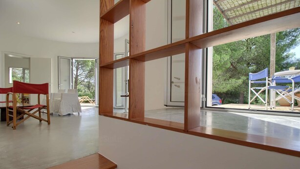 Un intérieur moderne avec un plancher en bois, une chaise pliante rouge et une grande fenêtre donnant sur l’extérieur.