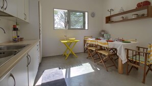 Une cuisine compacte avec une fenêtre, une table à manger avec des chaises et une petite étagère contenant des ustensiles de cuisine.
