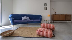 Un salon moderne avec un canapé bleu, une petite table d’appoint avec une lampe et un meuble en bois.