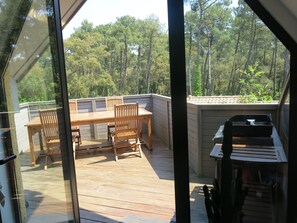 A wooden deck with a table and chairs, overlooking a forested area. - Large luxury apartment near the ocean with a terrace, nestled between the ocean, a golf course, and a lake (Seignosse)