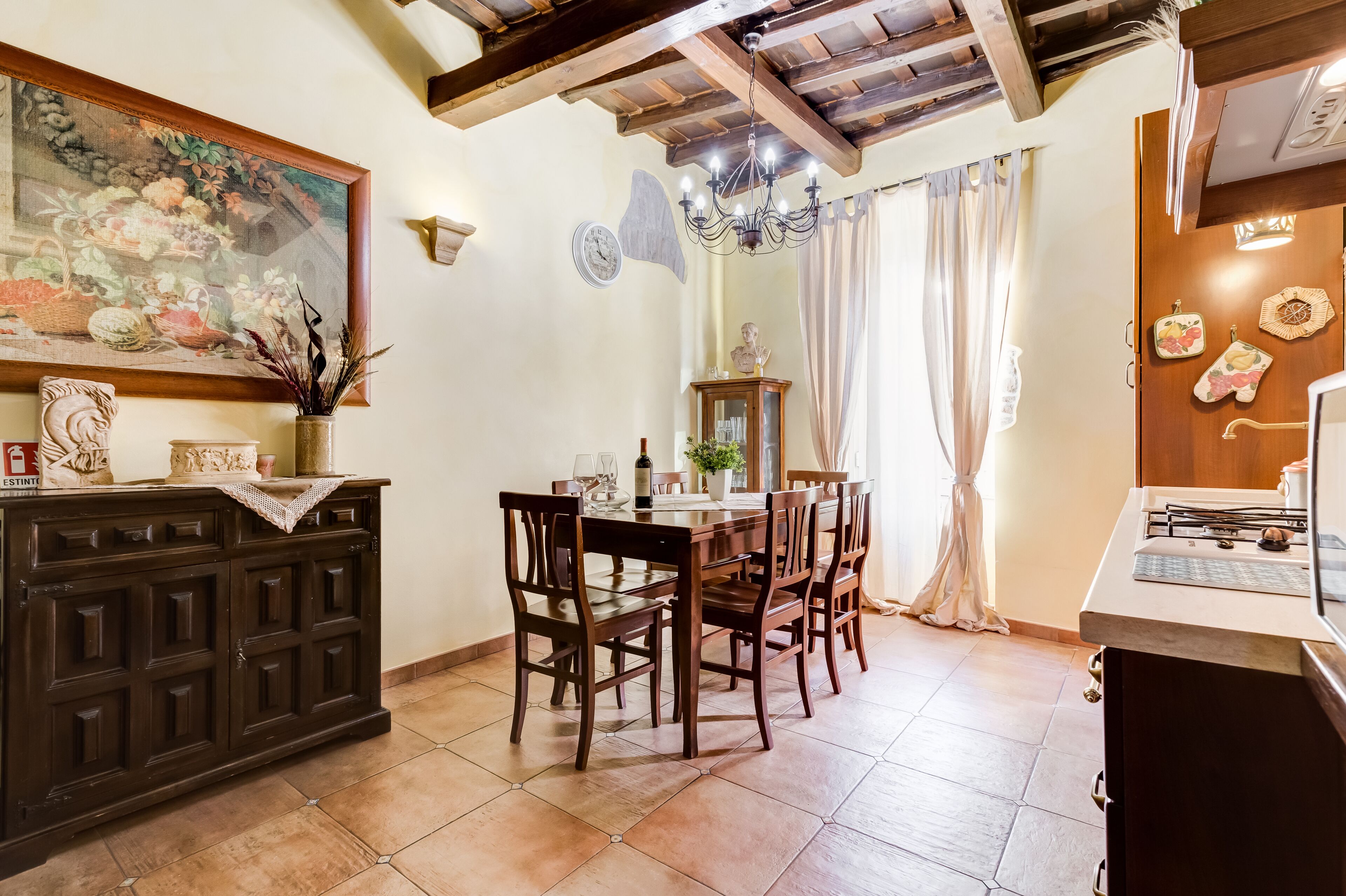 A dining area with a wooden table and chairs, a chandelier, and a painting on the wall.
